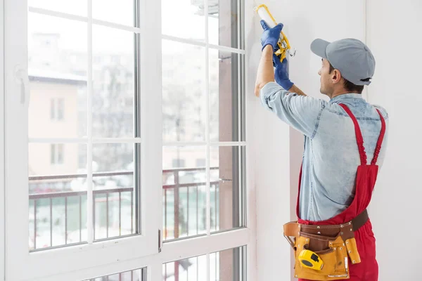 Construction worker putting sealing foam tape on window in house — Stock Photo, Image