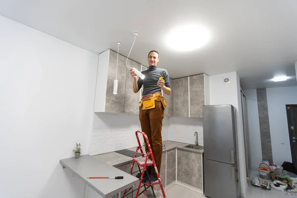 Electrician, a male electrician is standing on the stairs holding wiring in his hands and stripping, repairing light at home, repair work, call master, electrician man repairing light — Stock Photo, Image
