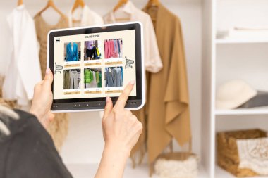 Teknolojileri iş kolay. Güzel genç kadın giyim mağazasında dururken gülümsemeyle onu dijital tablet kullanma.