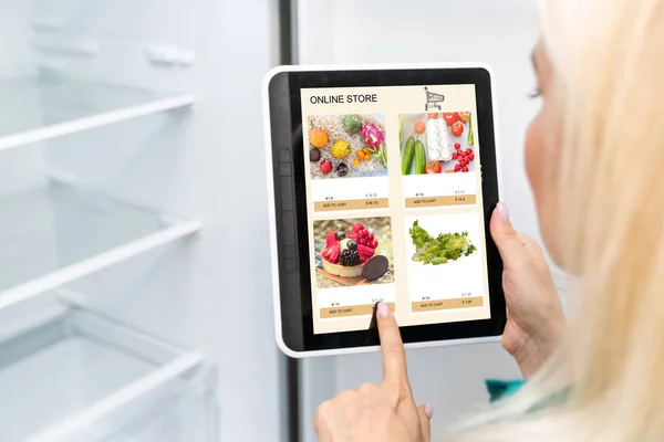 Woman shopping food online using a digital tablet at the kitchen, close-up view on a tablet screen. Concept of buying online using mobile devices.