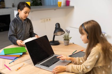 Online eğitim. Kulaklıklı iki liseli kız kardeş dizüstü bilgisayarlardan ders dinliyorlar. Okulda salgın ve karantina var..