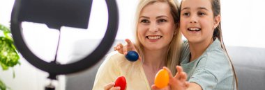 Genç mutlu kadın ve küçük kız akıllı telefonla yayın platformunda içeriği paylaşıyorlar. Milenyum vlogger çifti DIY Paskalya Dekorasyonu 'nun bir videosunu kaydediyor. Mutlu Paskalya videoları yapma kavramı.