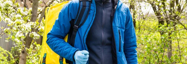 Νεαρός κούριερ με ιατρική μάσκα που παραδίδει φαγητό με κίτρινο θερμικό σακίδιο στην πόλη. Έννοια της υπηρεσίας παράδοσης τροφίμων — Φωτογραφία Αρχείου