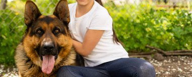 Güzel küçük bir kız ve bir Alman çoban köpeği gün içinde çimlerde oynuyorlar.