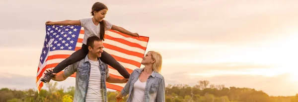 Vacker familj med den amerikanska flaggan i ett fält vid solnedgången. Självständighetsdagen den 4 juli. — Stockfoto
