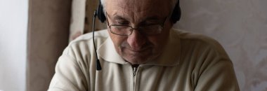 Dizüstü bilgisayar ve kulaklık kullanan kıdemli adam..