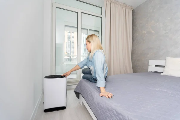 Žena zapíná a používá moderní čistič vzduchu v obývacím pokoji, čistič vzduchu je populární spotřebič - elektřina pro domácnost. Čistič vzduchu může pomoci vyčistit vzduch. — Stock fotografie