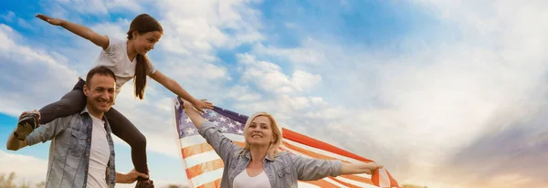 Patriotisk högtid. Lycklig familj, föräldrar och döttrar barn flicka med amerikansk flagga utomhus. USA firar 4 juli. — Stockfoto