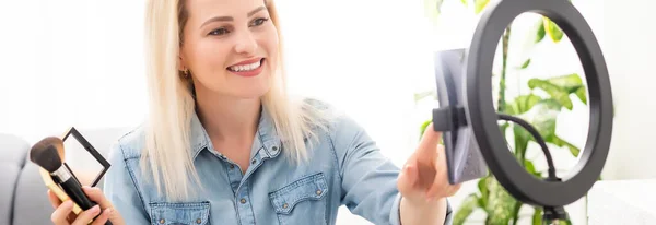 Blogger mujer grabando vídeo en smartphone e iluminándose con la lámpara de anillo en la mesa en la sala de luz — Foto de Stock