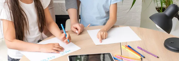 Mujer tutora o madre adoptiva ayudando a una linda niña de escuela caucásica haciendo la tarea sentada en la mesa. Niñera diversa y niño aprendiendo a escribir en cuaderno estudiando en casa — Foto de Stock