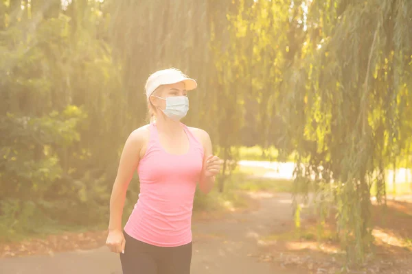 Pandemiczny koronawirus COVID-19 Kobieta na łące w stroju sportowym w masce ochronnej na wypadek rozprzestrzenienia się wirusa choroby SARS-CoV-2. Dziewczyna w masce ochronnej na twarzy. — Zdjęcie stockowe