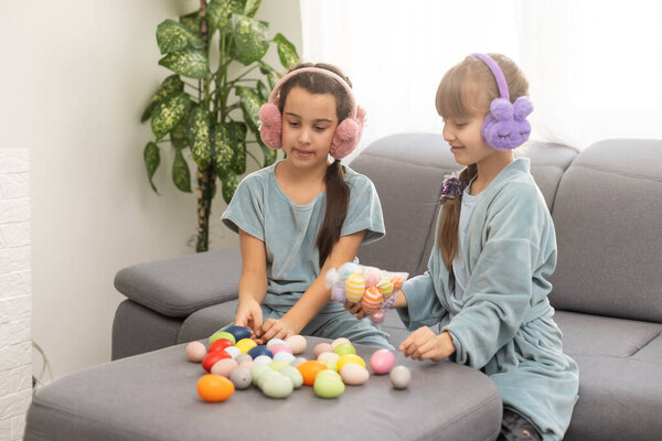 Две милые сестрички играют в охоту за яйцами на Пасху. Восхитительные дети празднуют Пасху дома.