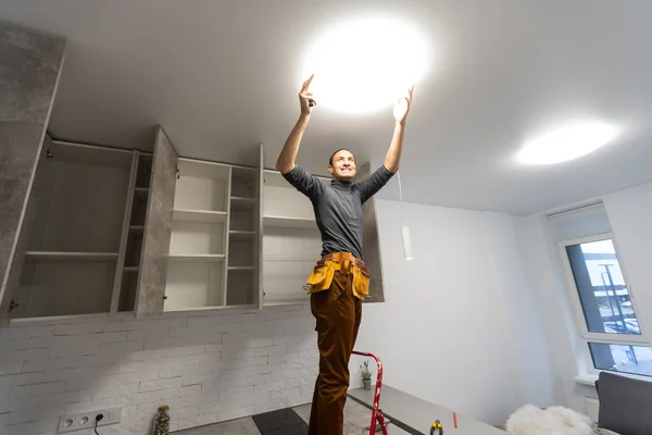 Konzeptualisierung der Deckenlampe im Raum. Ein glücklicher Mann auf einer Leiter zeigt zur Decke. — Stockfoto
