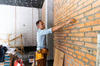Boş dairede genç bir profesyonel. Ölçüm bandıyla duvarı ölçüyor, notları doğruluyor. Onarım ve yenileme konsepti