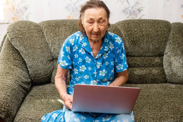 Donna anziana che guarda lo schermo di computer portatile durante videochiamata da casa — Foto Stock