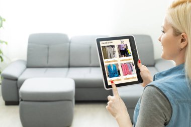 İnternet sitesinden dijital tabletle alışveriş yapan bir kadının arka planı. Kanepedeki bayanın üst görüntüsü. E-ticaret portalından ürün seçerken kızın ekrana dokunuşunun arka görünümü