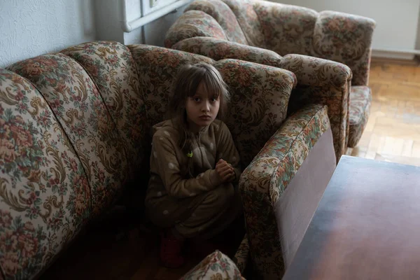 Lilla ukrainska flicka gömmer sig i soffan, ser förvirrad — Stockfoto