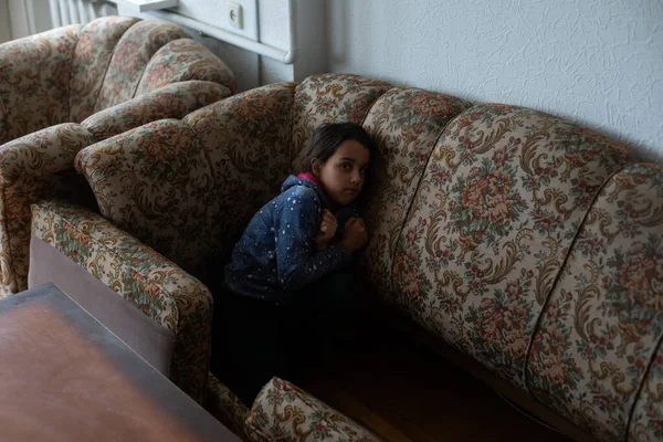 La chica, una caucásica, se ríe alegremente y se esconde en suaves almohadas en el sofá —  Fotos de Stock