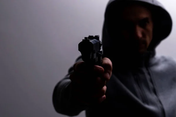Foto de un espeluznante criminal de terror con capucha negra sosteniendo pistola de revólver. —  Fotos de Stock