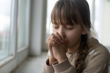 Pencerenin yanında dua eden küçük kız.