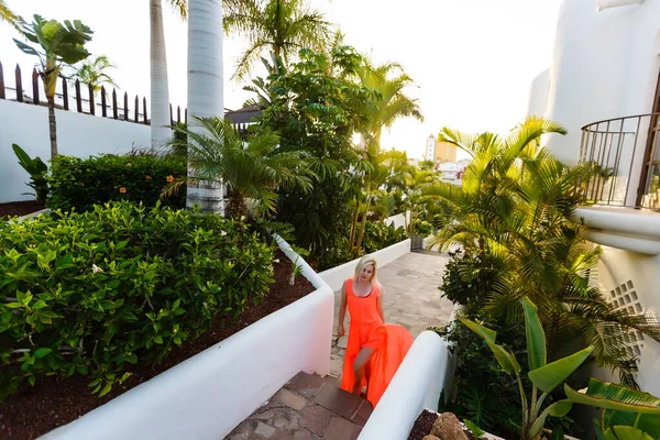 Stijlvolle jonge aantrekkelijke vrouw gekleed in een oranje-gekleurde gefotografeerd in de zomer op een achtergrond van palmbomen — Stockfoto