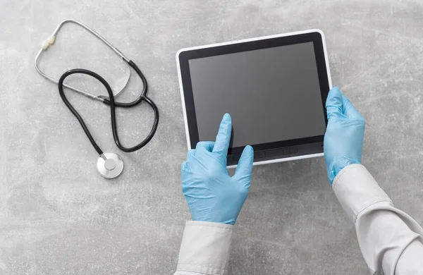 Κάτοψη των χεριών του γιατρού με τον υπολογιστή tablet. Καρδιακή εξέταση στο νοσοκομείο. Θεραπευτής κάθεται στο γραφείο με στηθοσκόπιο, ιατρικά γάντια. Εξέταση και συμβουλευτική στην κλινική — Φωτογραφία Αρχείου