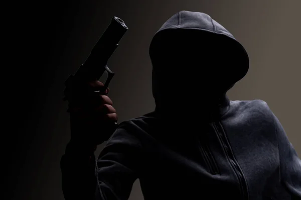 Foto de um criminoso de terror assustador com capuz preto segurando revólver. — Fotografia de Stock