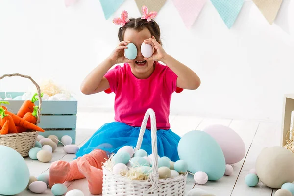 Готуємося до Великодня. Прекрасна маленька дівчинка тримає пасхальне яйце і посміхається з прикрасою на задньому плані — стокове фото