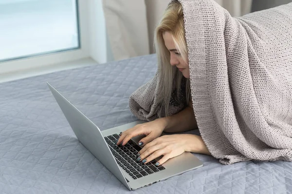 Kvinna med laptop täckt med filt i sovrummet — Stockfoto