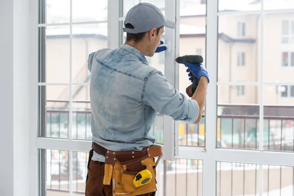 Handyman justera vit pvc plastfönster inomhus. arbetstagare som använder skruvmejsel för att reparera upvc fönster. läxunderhåll. — Stockfoto