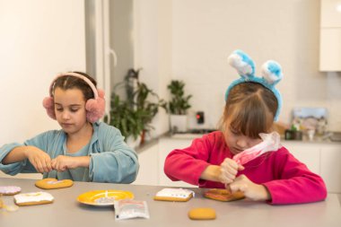 İki güzel kız kardeş, ahşap bir masada lezzetli pastalar süsleyip yiyorlar.