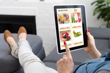 İnternet sitesinden dijital tabletle alışveriş yapan bir kadının arka planı. Kanepedeki bayanın üst görüntüsü. E-ticaret portalından ürün seçerken kızın ekrana dokunuşunun arka görünümü