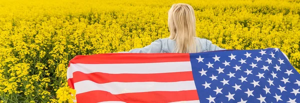 Vuxen kvinna som håller amerikansk flagga med stång, stjärnor och rand i ett gult rapsfält. USA flagga fladdrar i vinden — Stockfoto