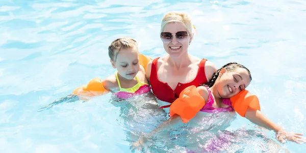 Familia feliz en la piscina, divirtiéndose en el agua, madre con niños disfrutando del parque acuático, resort de playa, vacaciones de verano, concepto de vacaciones — Foto de Stock