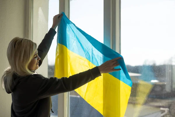 Uma mulher pendura uma bandeira de ucraniano na janela — Fotografia de Stock