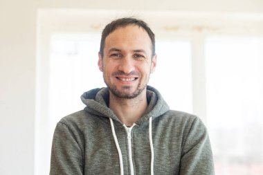 Sakallı, orta yaşlı bir adam kameraya bakıyor. Kafasında ve omuzlarında ciddi bir ifade var.