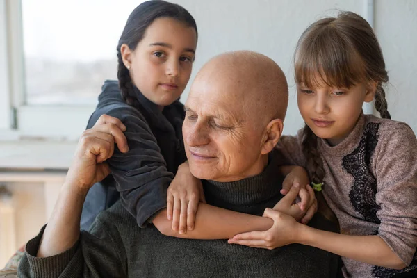 Grandfather and two granddaughters hugging on sofa at home — Stock Photo, Image