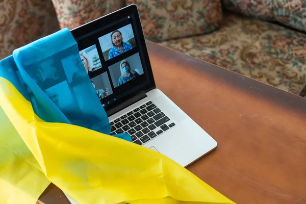 Онлайн за ноутбуком из дома на фоне флага Украины, военного положения в стране, онлайн-трансляции местных новостей, остановить войну и патриота — стоковое фото