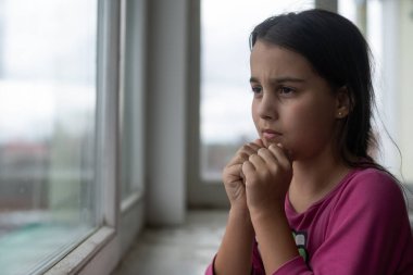 Pencerenin yanında dua eden küçük kız.