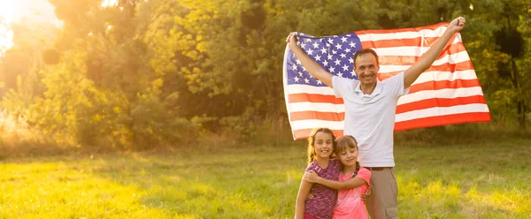Familia feliz en el campo con EE.UU., bandera americana en la espalda. — Foto de Stock