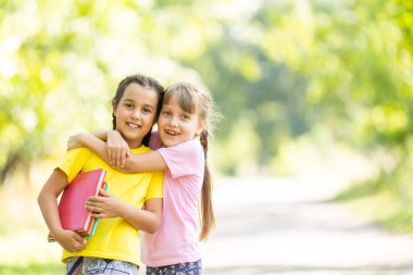 Parlak bir sonbahar gününde, elinde kitaplarla şehir parkında iki küçük kız öğrenci.