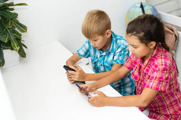 Dos niños preescolares niño y niña se sientan juntos y juegan con el teléfono inteligente —  Fotos de Stock