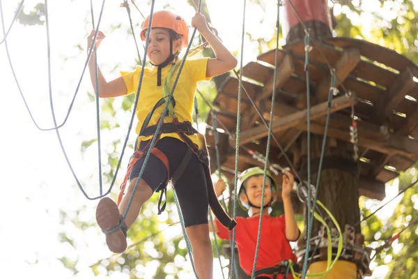 Niño en el parque de aventura forestal. Los niños suben por el sendero de cuerda alta. Agilidad y escalada centro de diversiones al aire libre para niños. Niña jugando al aire libre. Patio de la escuela patio con cuerda manera . — Foto de Stock