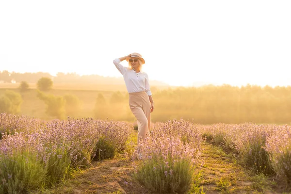 Fiatal szőke utazó szalmakalapot visel a levendula mezőn, levendula virágokkal körülvéve.. — Stock Fotó