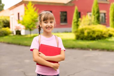 Okula dönelim. Eğitim konsepti. Okula giderken gülümseyen tatlı bir kız öğrenci. Sırt çantasıyla kitapları tutan mutlu küçük kız çocuğu..