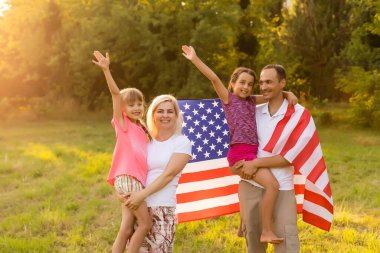 Gün batımında buğday tarlasında Amerikan bayrağı taşıyan mutlu bir aile. Bağımsızlık Günü, 4 Temmuz.