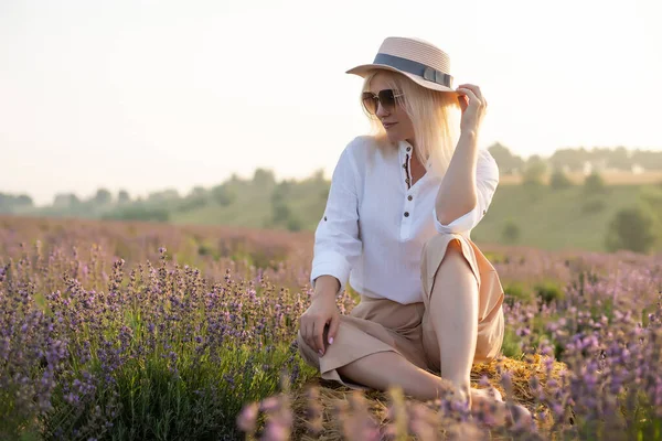 若いブロンドの女性旅行者はラベンダーの花で囲まれたラベンダー畑でわら帽子をかぶって. — ストック写真