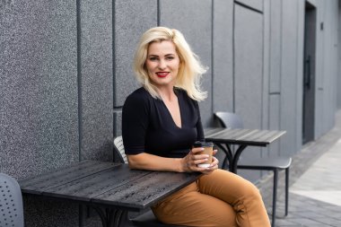 Havalı sarışın kadın terasta oturmuş kahve içiyor, hafta sonunun tadını çıkarıyor..