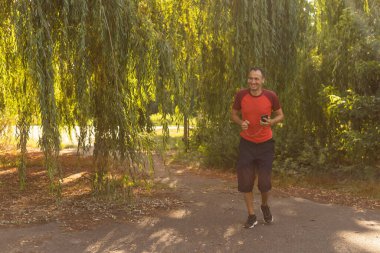 Parkta koşan bir adamın portresi. Kulaklıkla müzik dinlerken koşan gülümseyen bir adamın fotoğrafını çek.