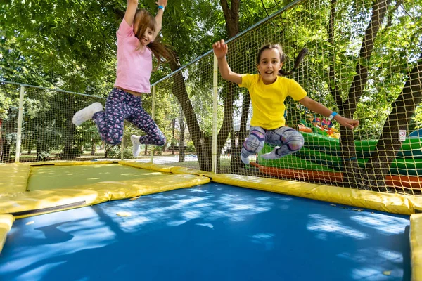 Chicas lindas divirtiéndose al aire libre. Saltar sobre trampolín en zona infantil. Parque de atracciones —  Fotos de Stock